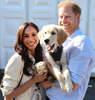 Meghan Markle wears a cream jacket while cuddling a puppy Prince Harry is holding at the Invictus Games Düsseldorf 2023 on September 15, 2023