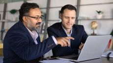 Two businessmen look at a laptop together in an office.