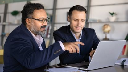 Two businessmen look at a laptop together in an office.