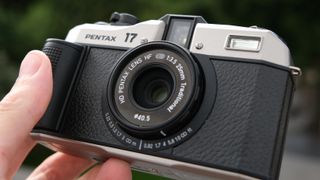 Close up of the lens on a Pentax 17 film camera held in a hand outside