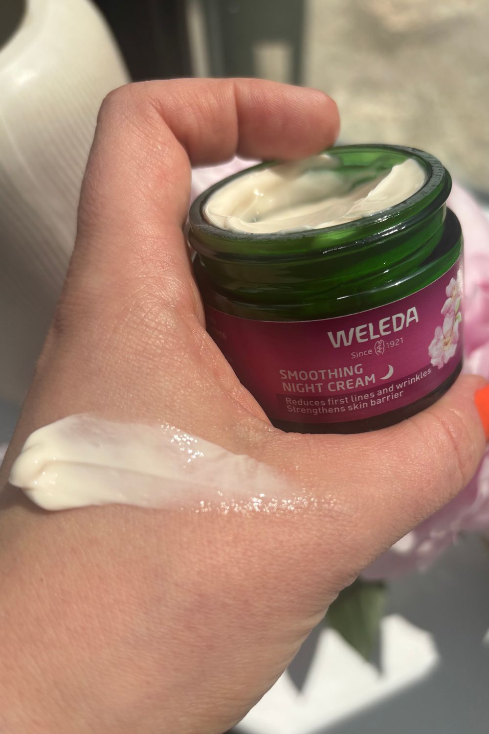 a hand holding the weleda wild rose and white tea night cream with a smear of product