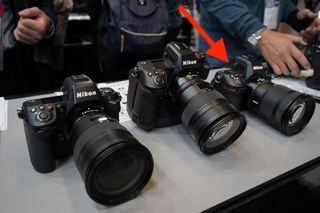 Three Nikon cameras sitting next to each other on a bench with an arrow pointing to one