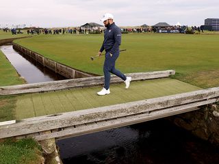 Tyrrell Hatton walking across a bridge holding his putter