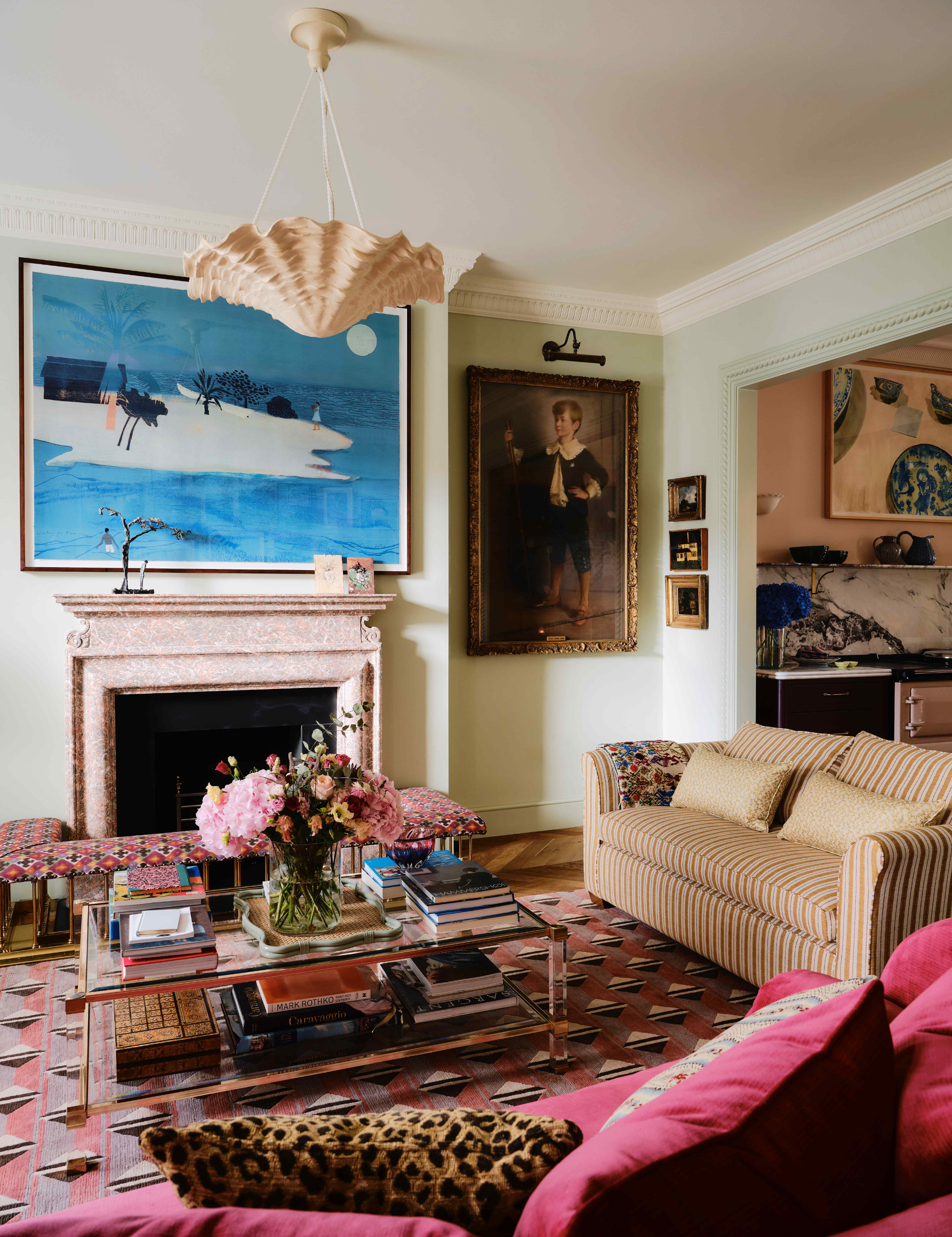 Layered living room featuring a mauve and magenta geometric rug, glass two-tier coffee table, striped sofa, and collected wall art