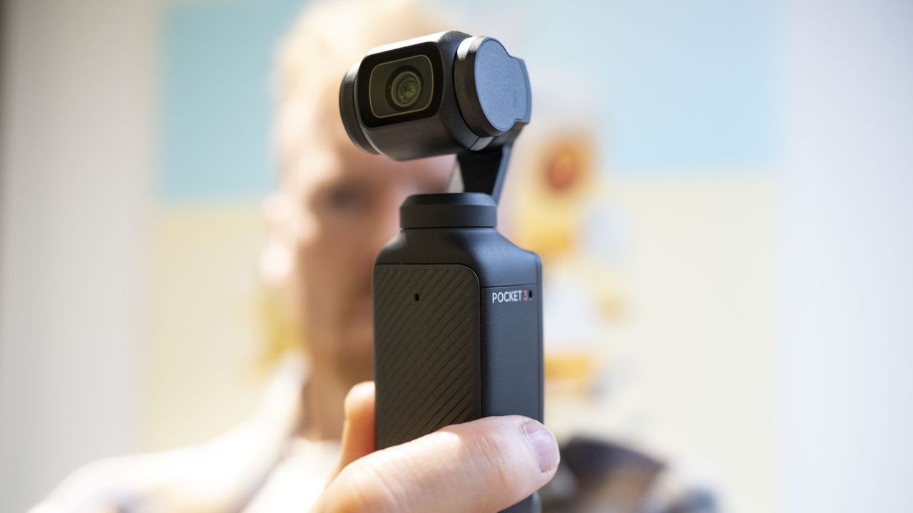 DJI Osmo Pocket 3 vlogging camera in usr's hand, with them blurred in the background