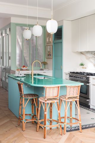 white kitchen with a teal kitchen island that has a lava stone worktop. There are rattan bar stools around the island