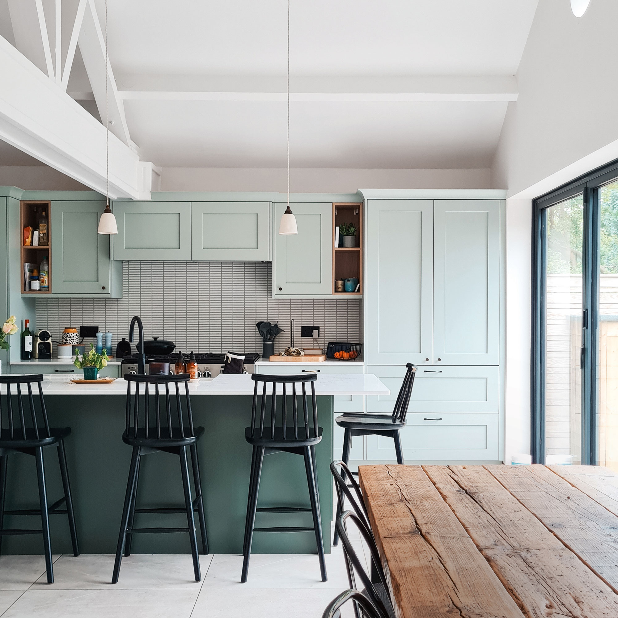 Green kitchen cabinets with black bar stools around kitchen island