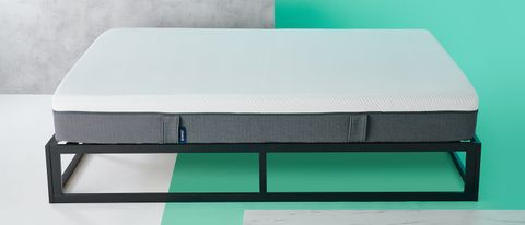The Emma Mattress shown on a black metal bed frame and placed against a green wall