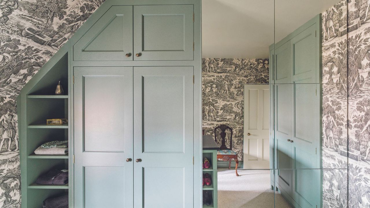 Dressing room with built-in cupboards and mirror tiles on one wall. Grey toile wallpaper.