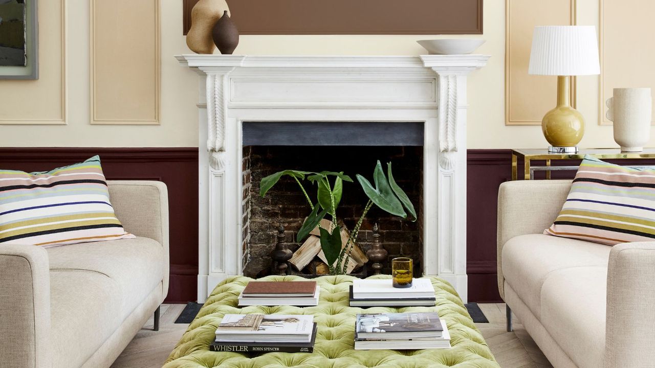 corner of traditional living room with white fireplace, beige panelled walls, cream sofas with striped cushions and green ottoman