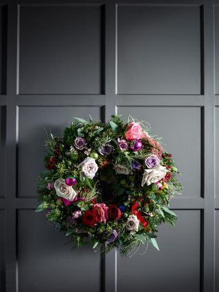 Wreath hanging on a dark gray door. The wreath has many different fresh roses and flowers dotted within it