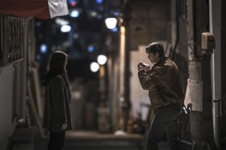 Two people stand in a Seoul alley, a woman (left) with her arms down and a man (right) in a fighting stance. From left, Han So-hee as Yoon Chae-ok, Park Seo-jun as Jang Ho-jae in Gyeongseong Creature S2.