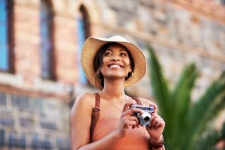 The best travel camera, woman in a hat holding a camera and smiling