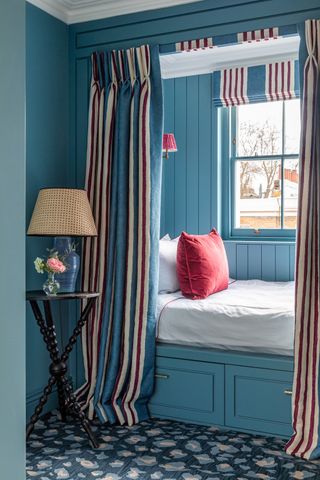 Blue room with bed built in behind curtains with drawers below