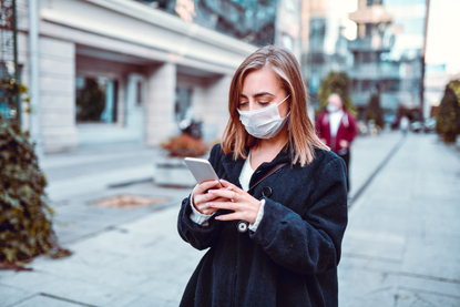 woman walking down the road in face mask looking at phone