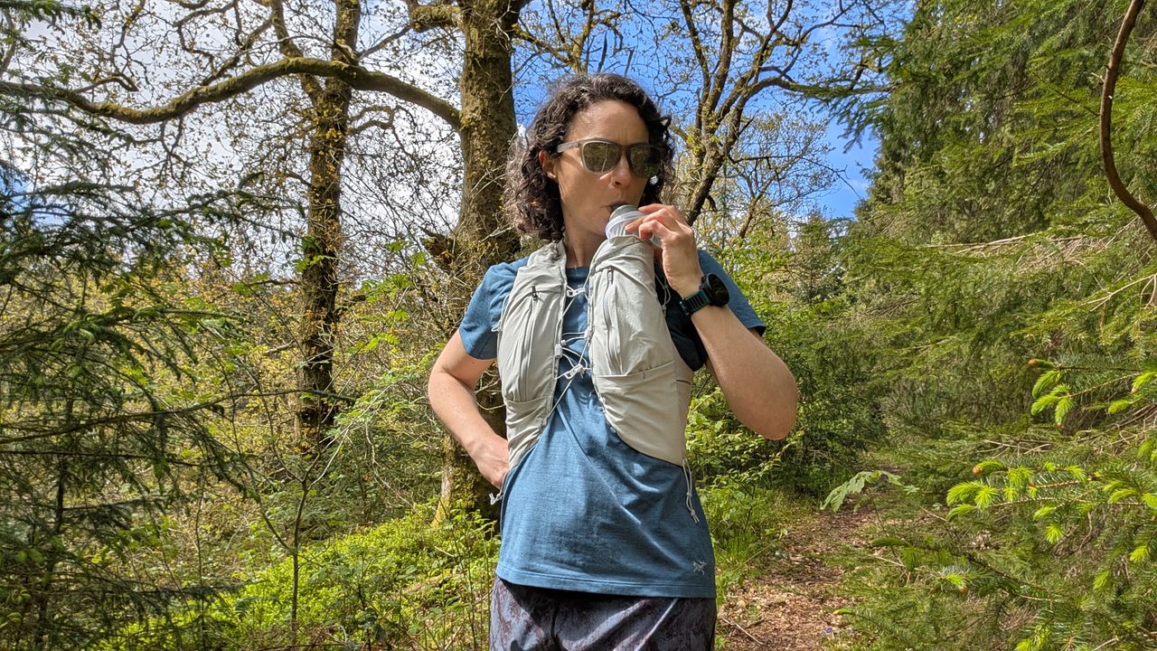 A woman trail runner drinks water from a bottle in her Montane Gecko hydration vest