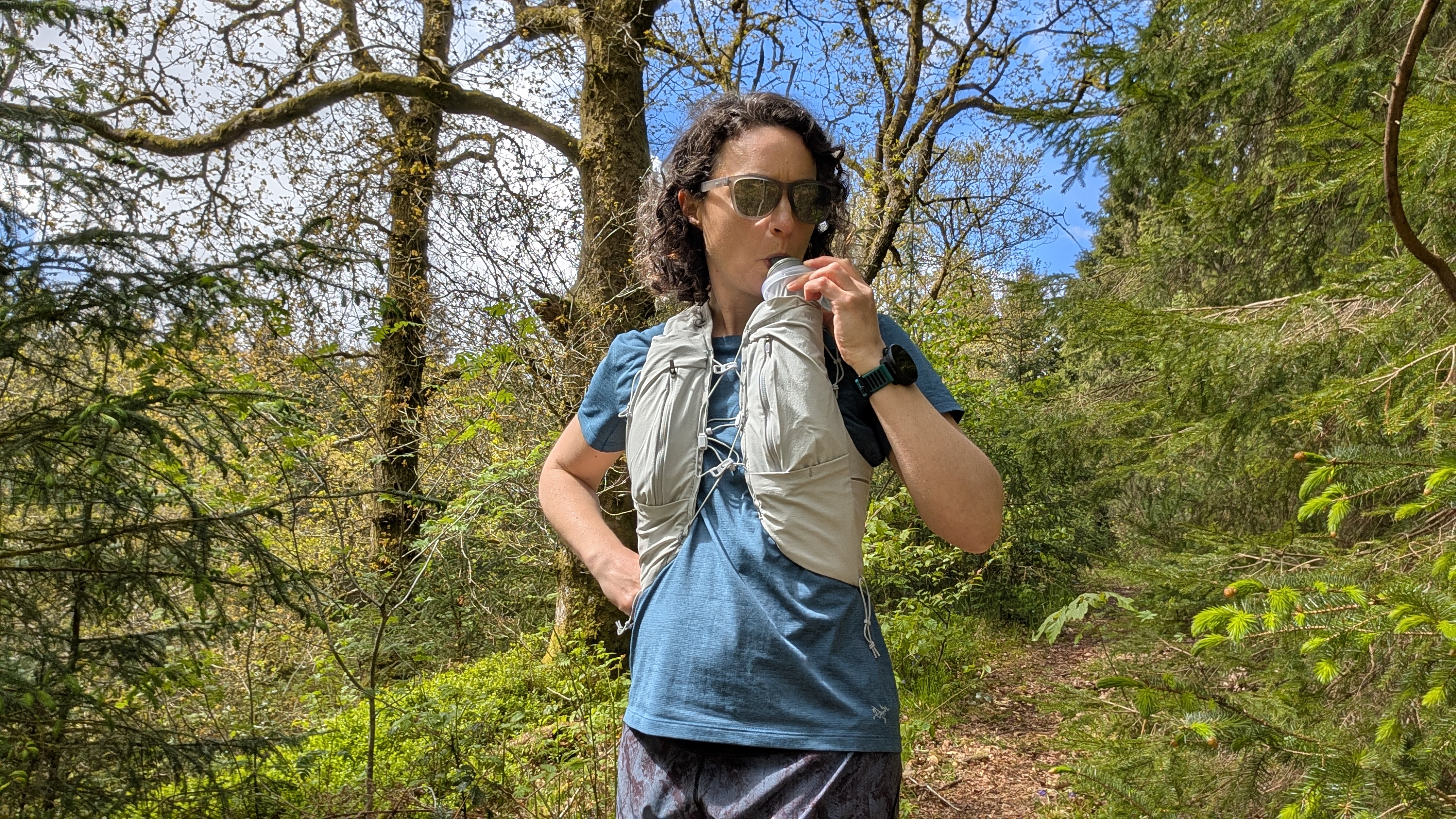 A woman trail runner drinks water from a bottle in her Montane Gecko hydration vest