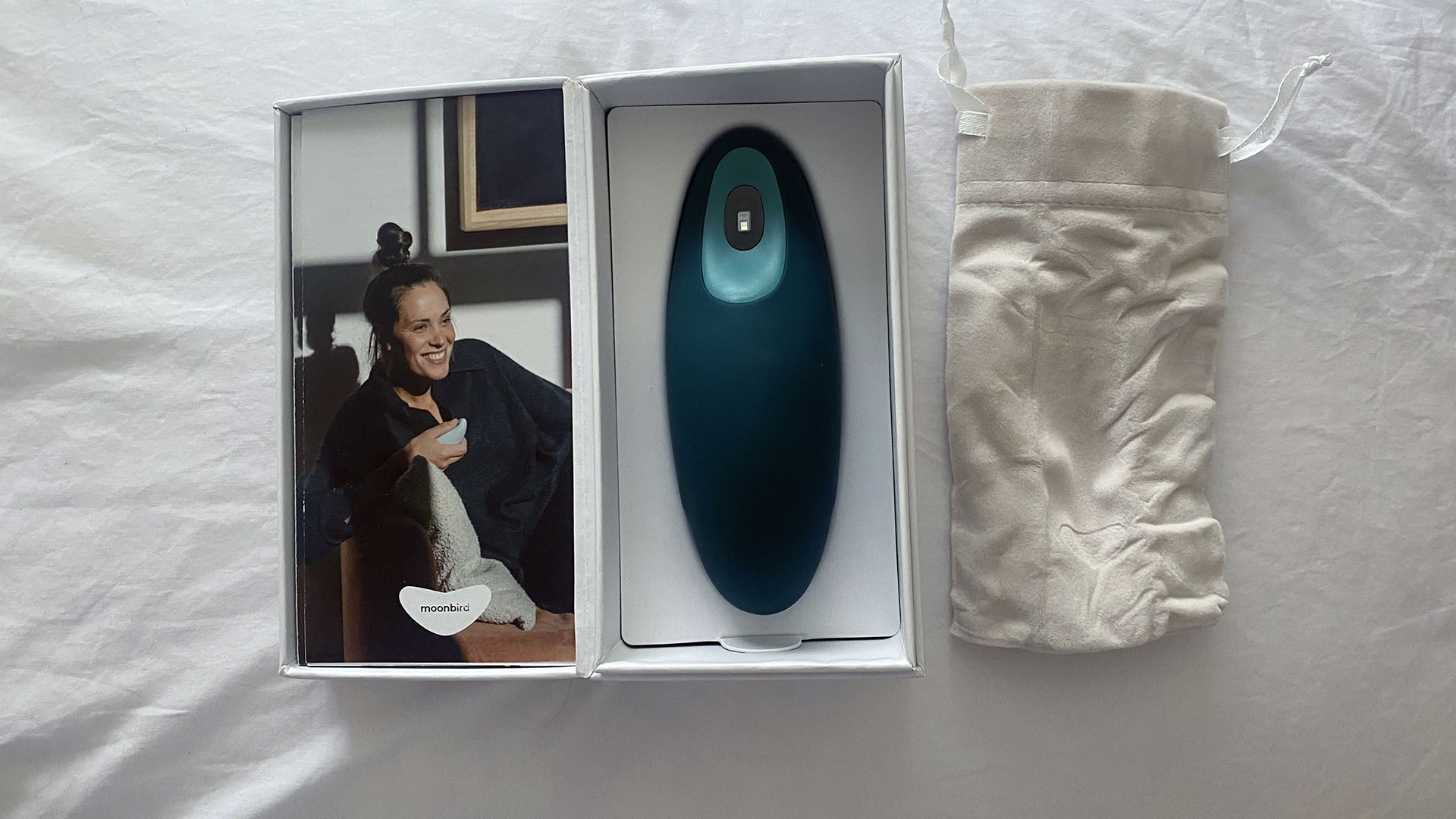 The moonbird in it's box on a white bed sheet. Next to it is the small personal puch the moonbird can fit into for travel