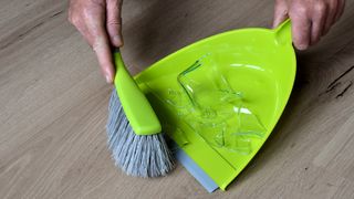 Lime green dustpan and brush sweeping up a broken glass on wood floor.