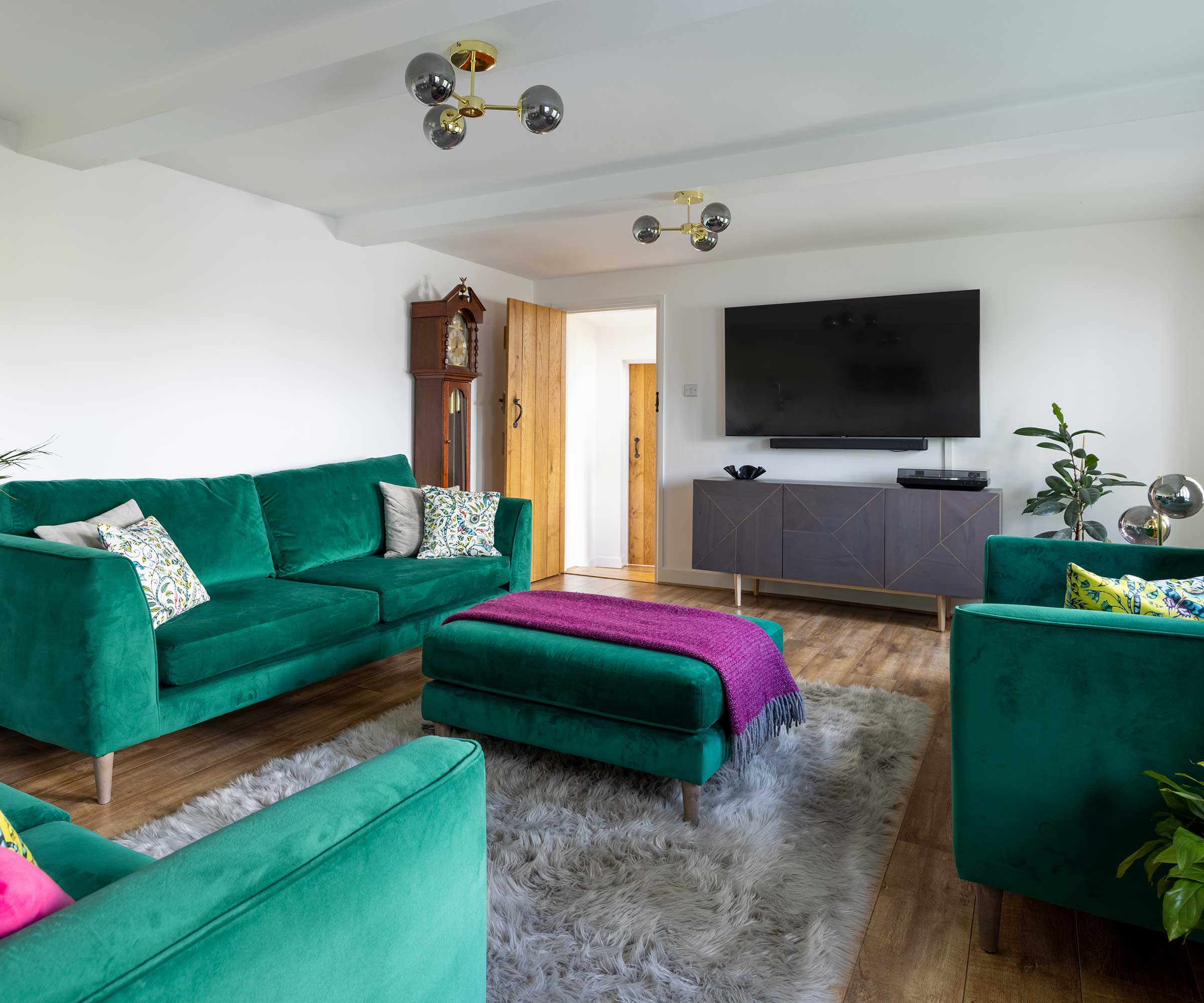 living room in a cottage with green velvet sofas, a TV and a grey rug on the floor