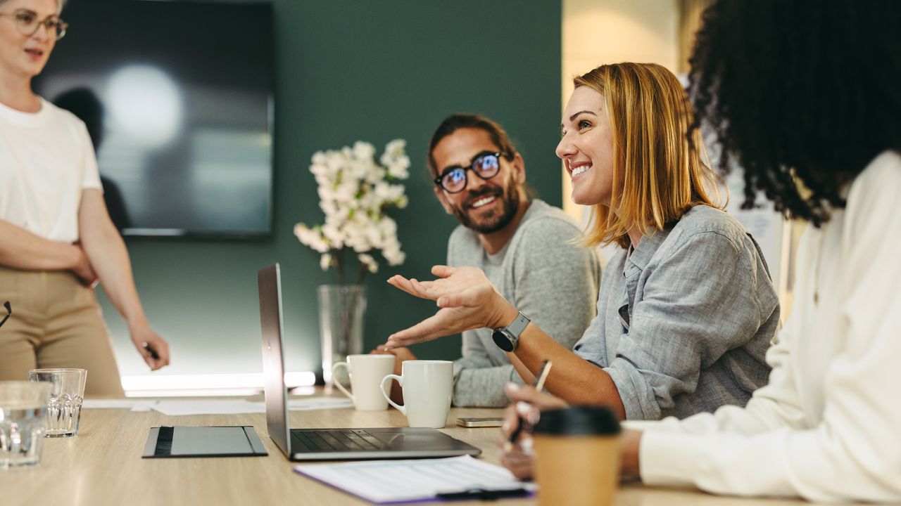 A smiling employee talks to her happy colleagues during a meeting in a conference room.