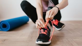 A woman laces up her trainers to exercise early in the day for better sleep at night