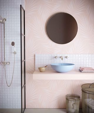 Light pink bathroom scheme with pink palm wallpaper feature wall, pastel ceramic sink and round wall mirror