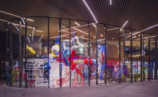 Exterior view of Charles Jeffrey's colourful 'The Come Up' exhibition and linear lighting through Now Gallery’s windows at night