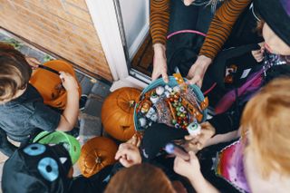 Overhead view of a group of children at a front door taking sweets from a bowl at Halloween
