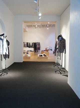 Tres Bien Shop, Sweden. A hallway into a clothing store with clothing displayed on mannequins at the entrance, a dark grey carpet and spotlights on the roof.