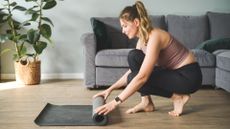 Woman rolling out yoga mat for the bird dog exercise in living room