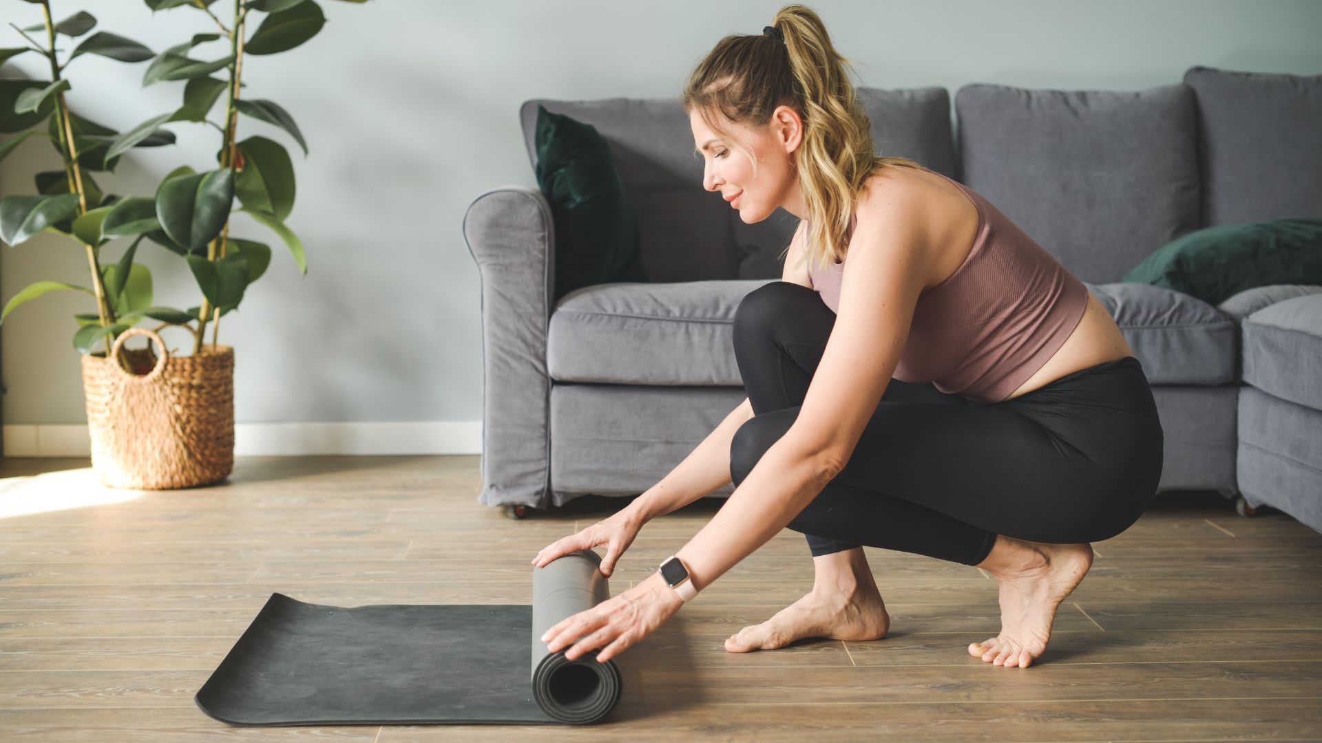 Woman rolling out yoga mat for the bird dog exercise in living room