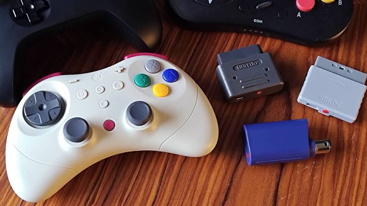 Gulikit Elves 2 Pro controller on woodgrain table next to 8Bitdo Retro Receivers for SNES, PS1, and GameCube.
