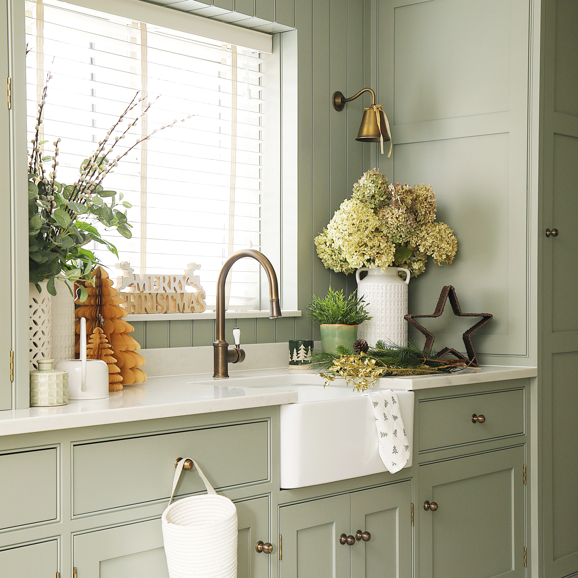 a utility room with sage green cabinetry and a Belfast sink decorated for Christmas