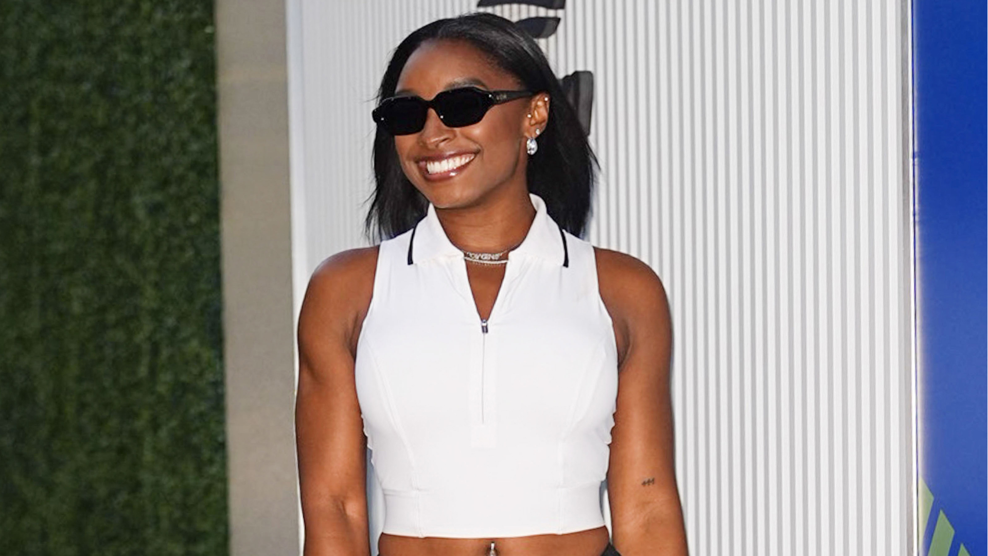 Simone Biles wearing a bob haircut a halter neck zip-up top and black sunglasses.