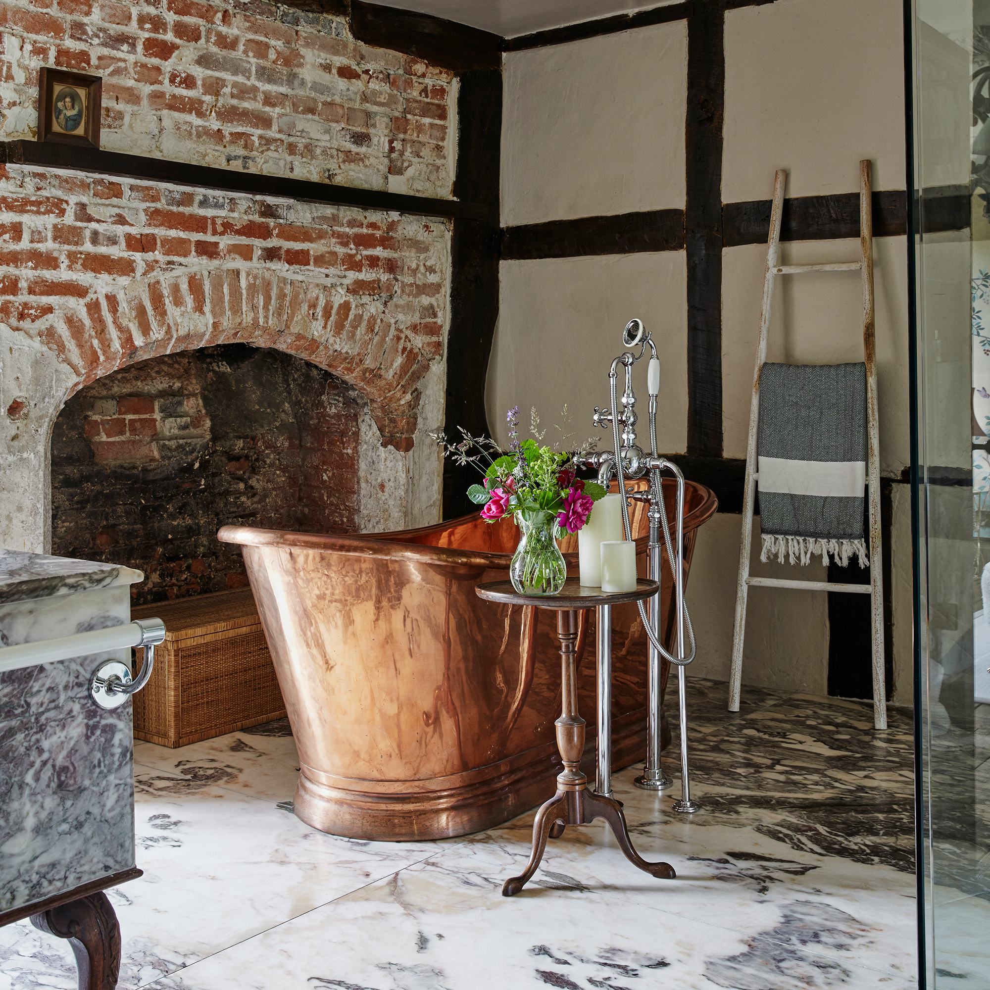 country bathroom with original fireplace and exposed brickwork, copper bath and marble floor tiles