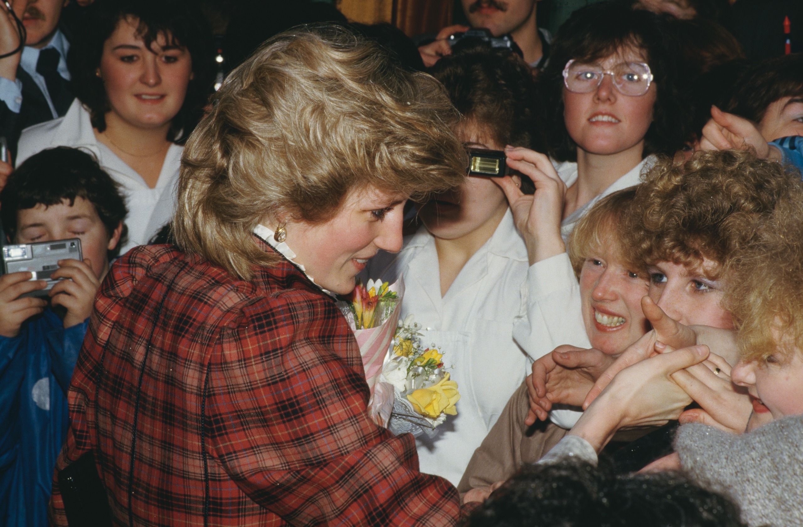 Princess Diana shaking hands with fans wearing a red plaid suit