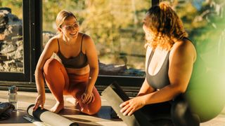 Woman rolling up yoga mat and talking to friend in class, laughing and smiling in the sun