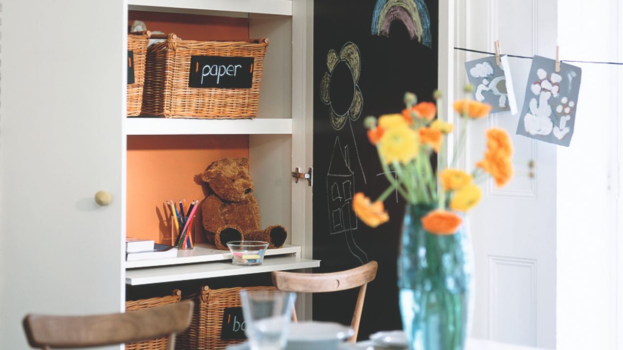 A toy storage unit with labelled baskets and a blackboard with drawings in a dining rooms