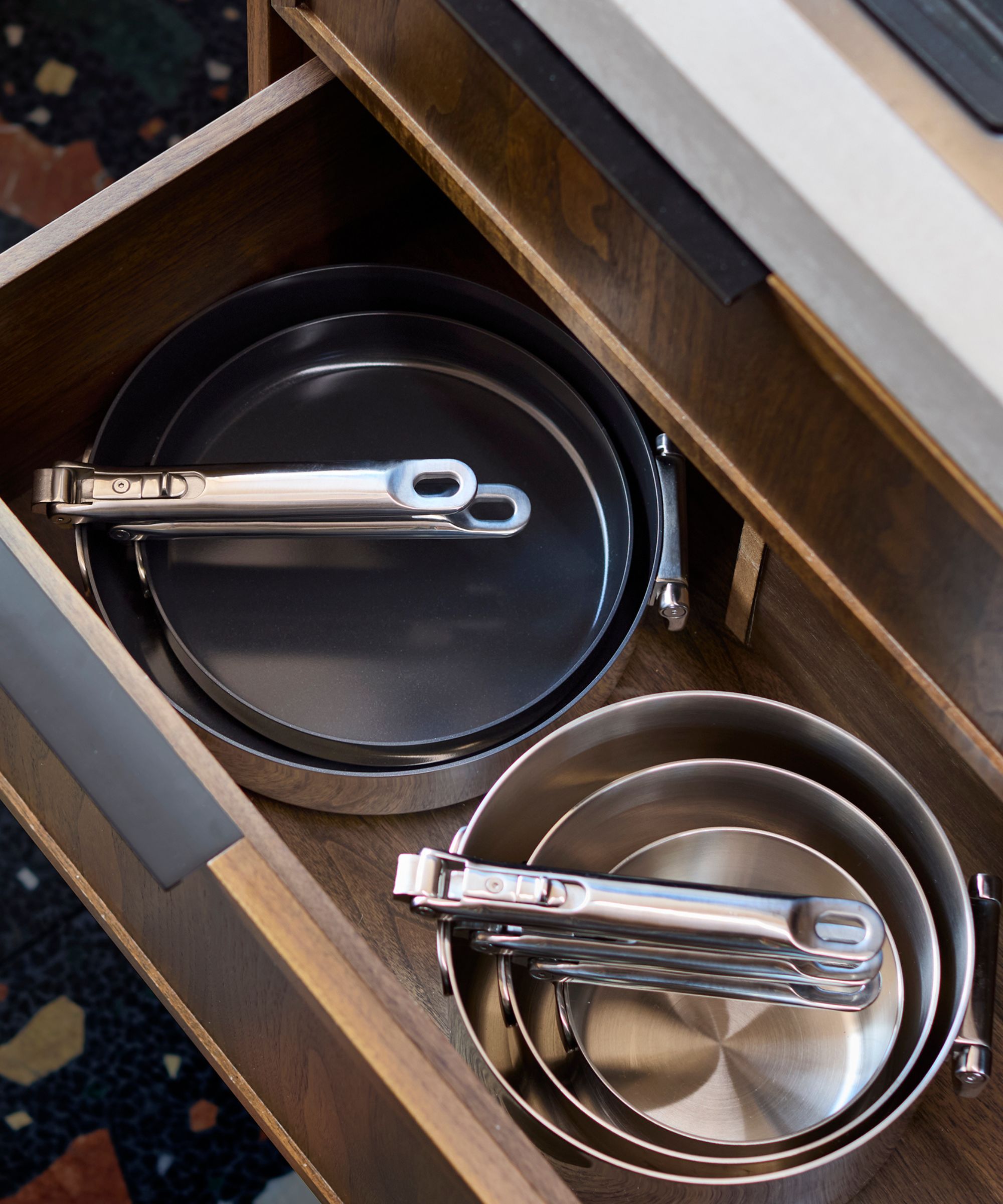 Open drawer containing stainless steel and non-stick frying pans with foldable handles