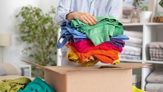 A person decluttering clothes in a cardboard box