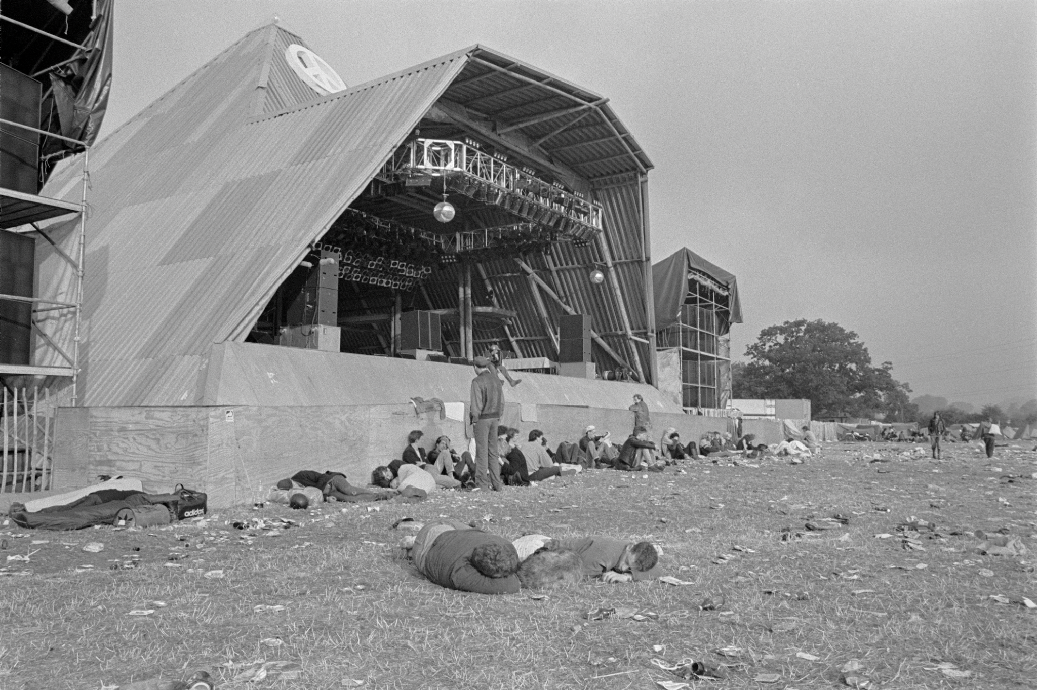 An empty Pyramid stage with people asleep in front of it at Glastonbury in the 1980s