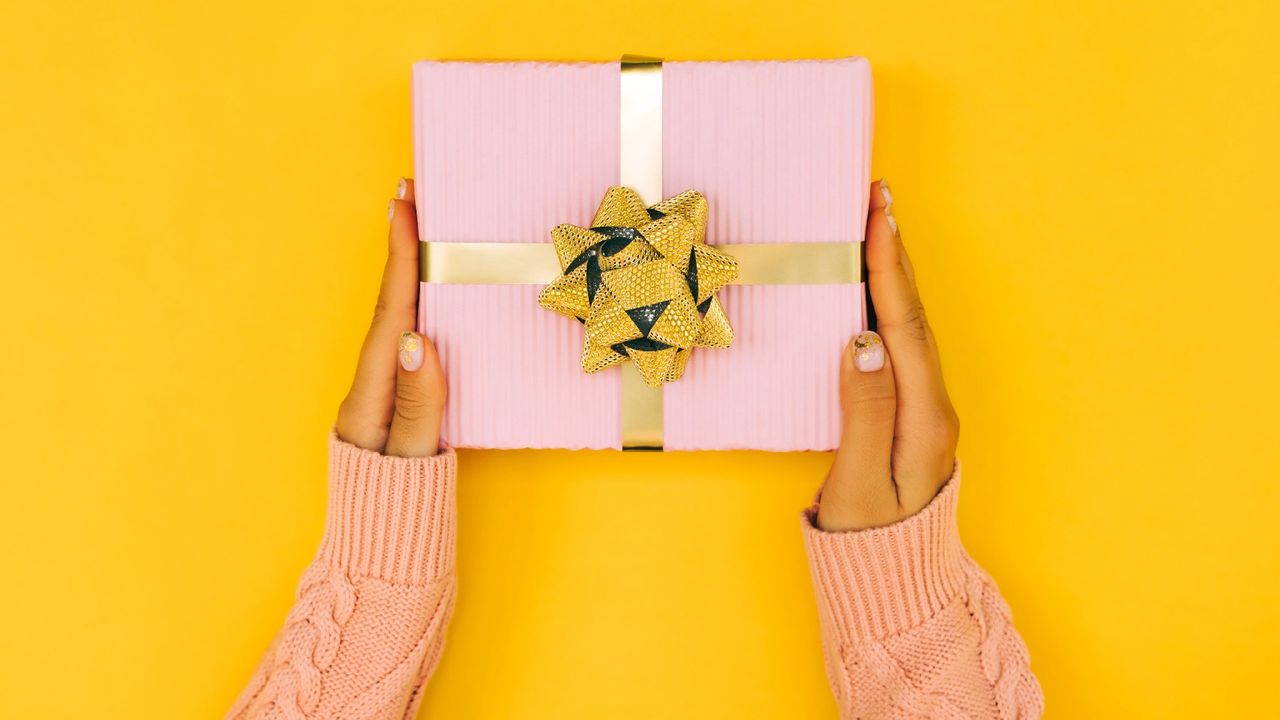 A woman&#039;s hands holding a mother&#039;s day gift on a yellow background