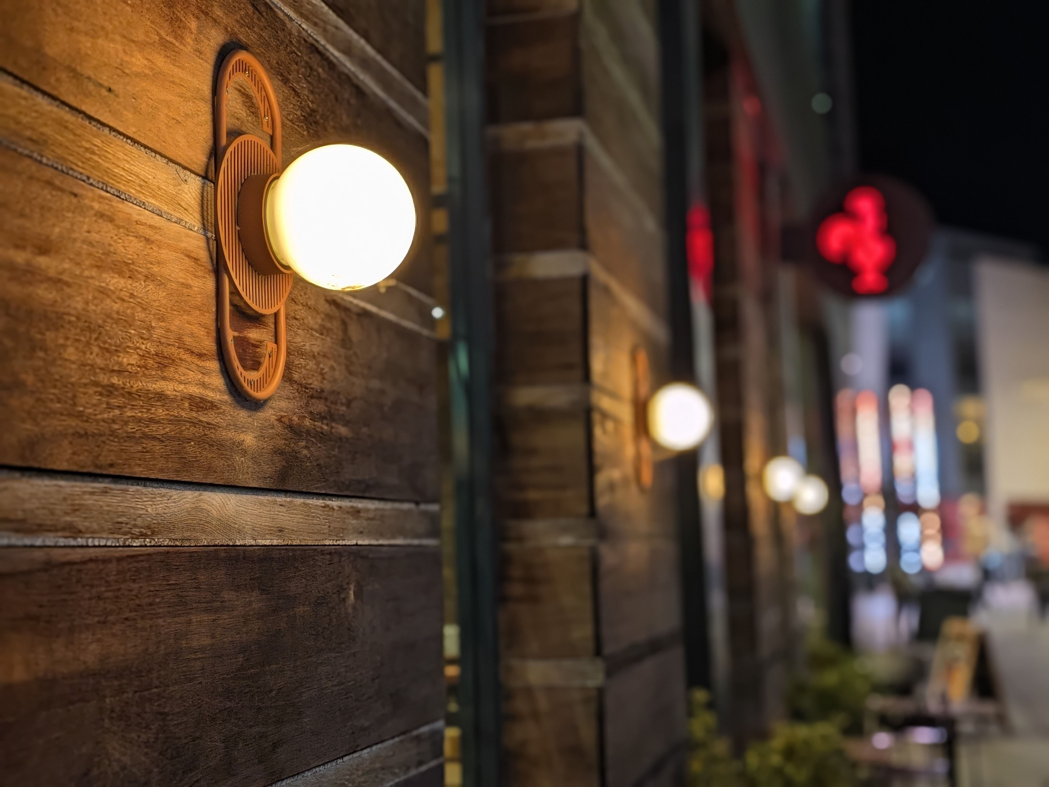 Close-up of a glowing globe wall light mounted on wooden paneling, with colorful city lights blurred in the background.