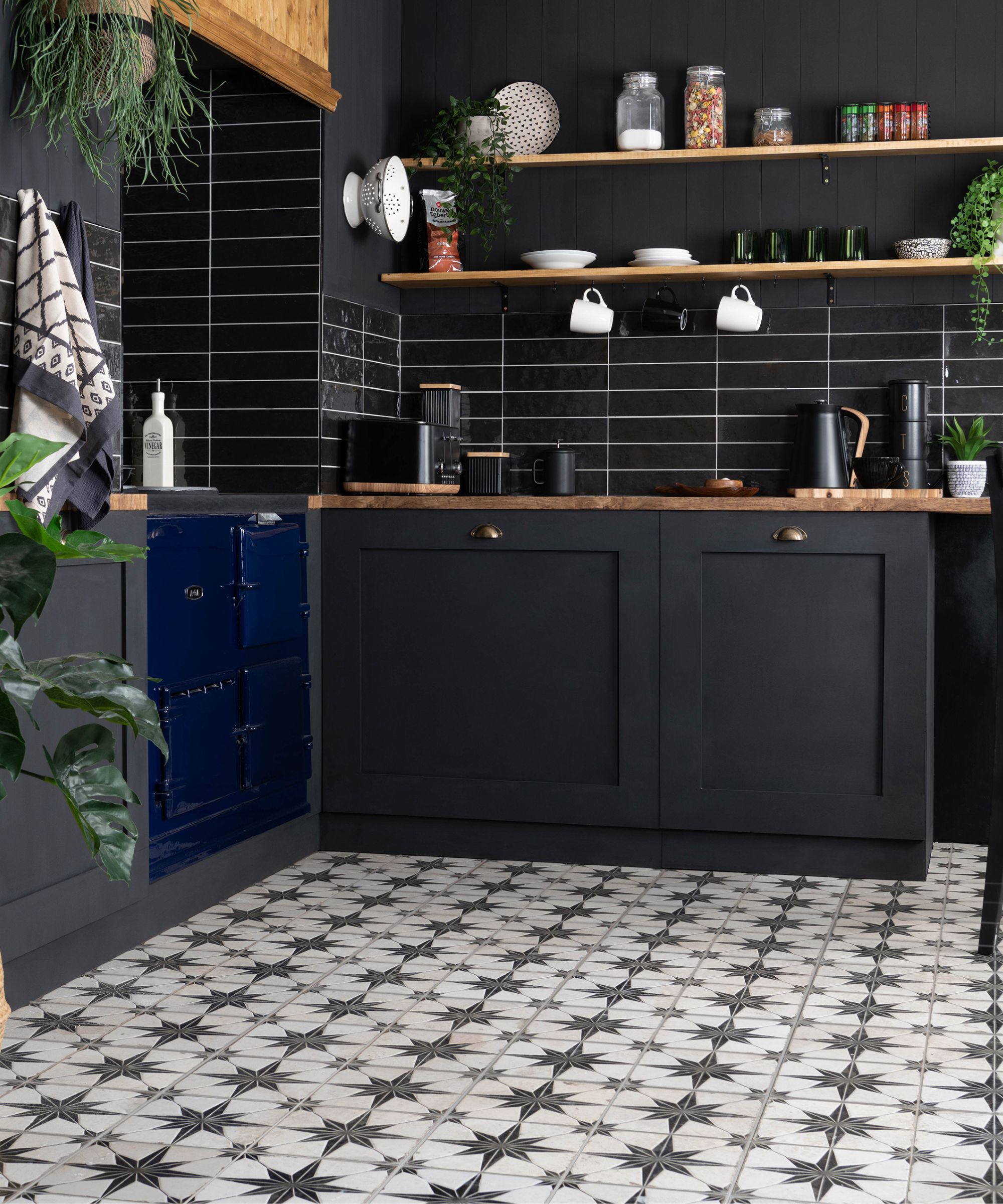 A repeating geometric star motif in black and soft white spans the floor, creating a strong graphic base. The tiles are square, laid in a neat grid, with crisp lines that contrast against the matte dark cabinetry. The pattern feels rhythmic and structured, with the black elements anchoring the lighter background.