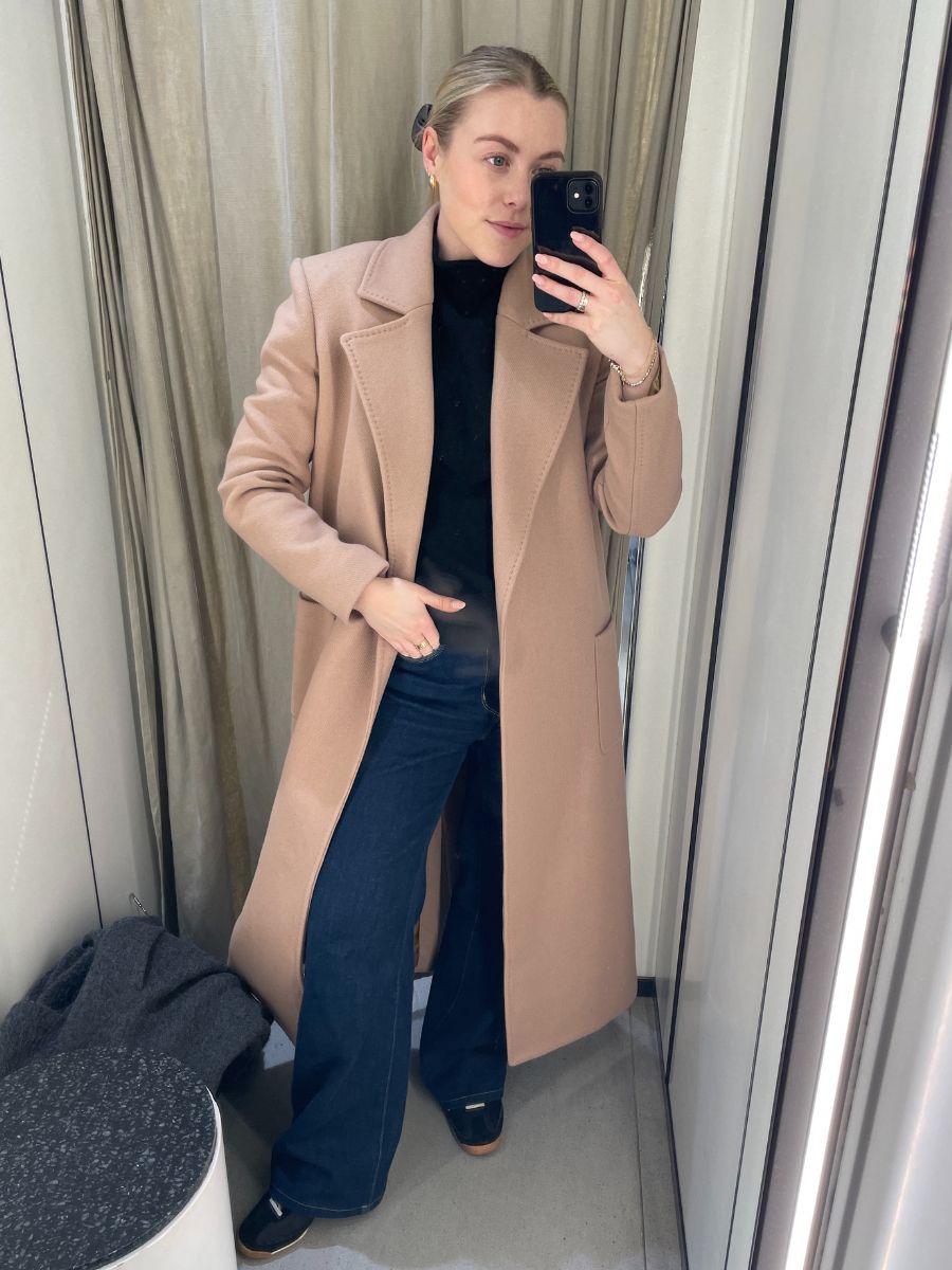Woman wears beige coat, black top and blue jeans