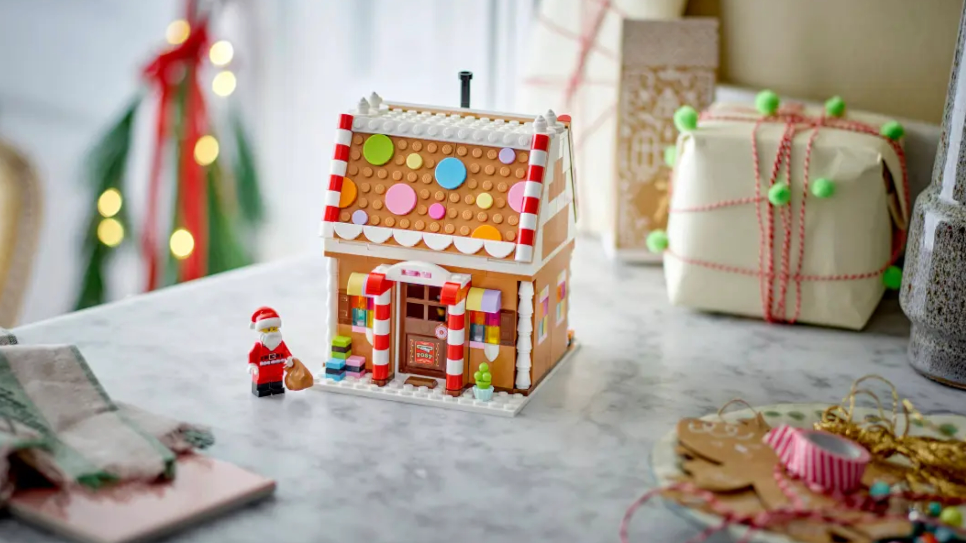 Lego Festive Gingerbread House and Santa minifigure on a granite surface, beside decorating materials