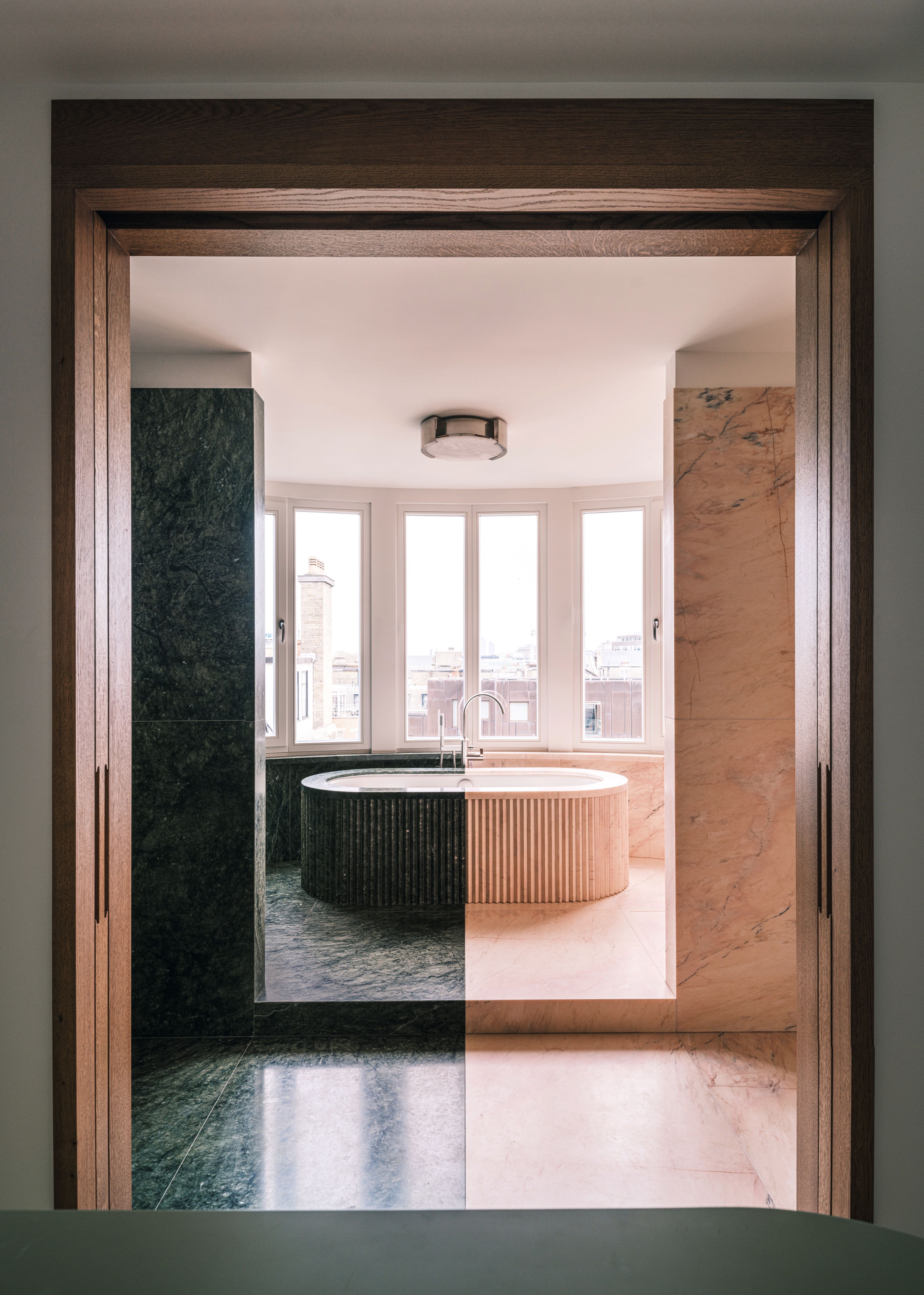 bath tub in bathroom where half the room is covered in black marble and the other half is covered in pale pink marble