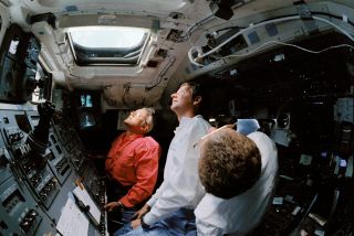 Three astronauts monitor Hubble deployment from within space shuttle Discovery.