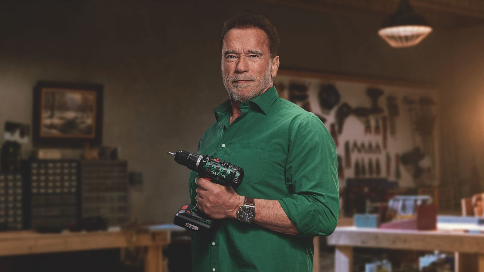 Arnold Schwarzenegger holding a drill while wearing a green shirt